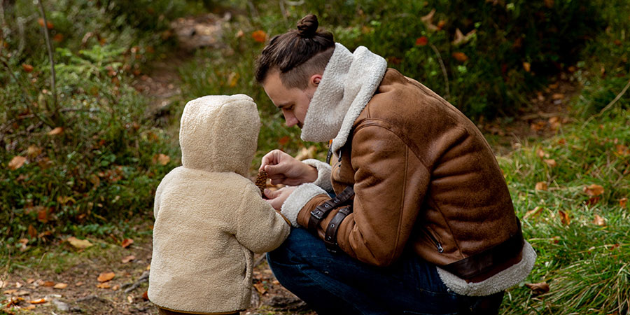 En man sitter på huk bredvid ett litet barn i skogen. 